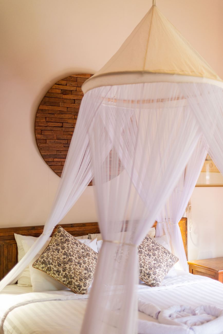 A double bed under a white mosquito net canopy, with a round reclaimed-wood panel behind it