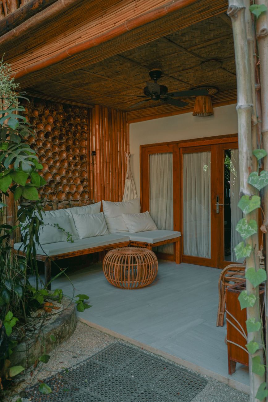 A covered terrace with a white cushioned sofa, bamboo walls and a rattan side table